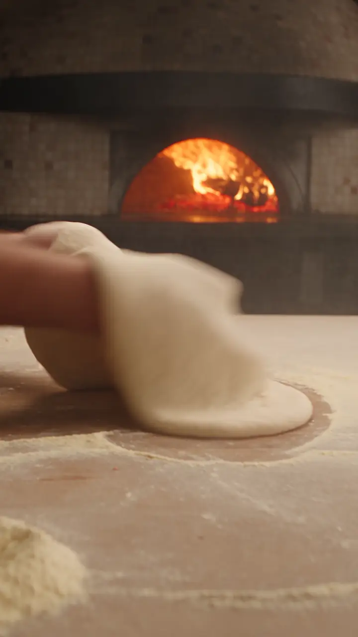A pizza base being stretched by hand in front of a wood fired oven